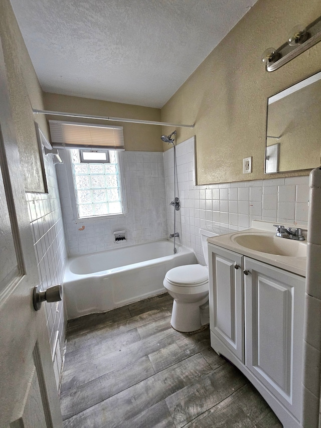 full bathroom featuring tiled shower / bath, wood-type flooring, tile walls, toilet, and a textured ceiling