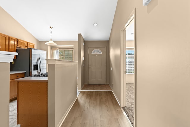 kitchen with lofted ceiling, decorative light fixtures, stainless steel fridge, and light wood-type flooring