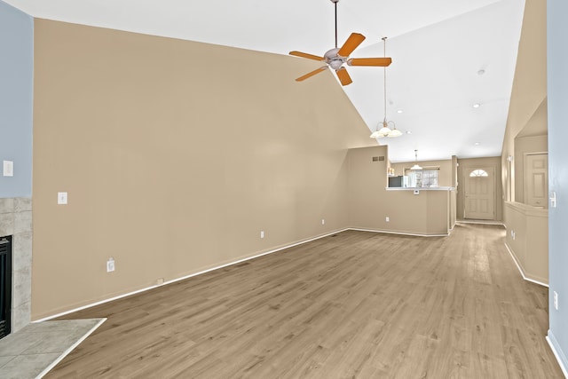 unfurnished living room with ceiling fan, high vaulted ceiling, a tiled fireplace, and light hardwood / wood-style floors