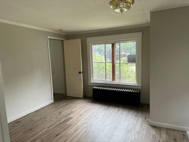 empty room with radiator heating unit, hardwood / wood-style floors, and ornamental molding