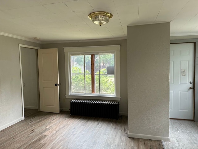 spare room featuring light wood-type flooring, crown molding, and radiator heating unit