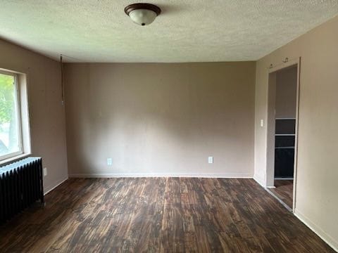 unfurnished room with dark wood-type flooring, a textured ceiling, and radiator heating unit