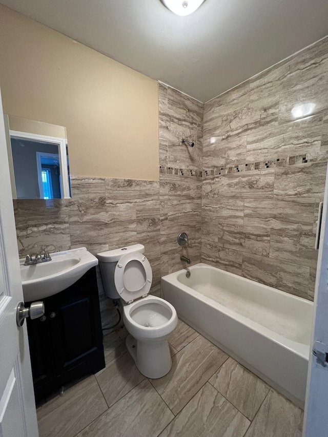 full bathroom with tile walls, tiled shower / bath, vanity, and toilet