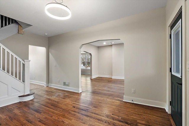 interior space with arched walkways, visible vents, baseboards, stairway, and dark wood-style floors