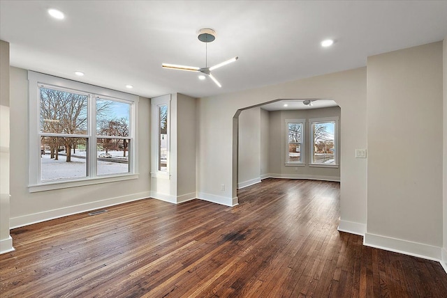 spare room featuring arched walkways, dark wood finished floors, recessed lighting, visible vents, and baseboards