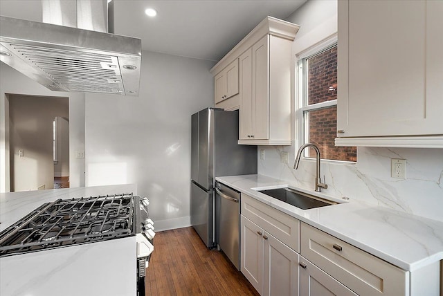 kitchen with light stone countertops, wall chimney range hood, stainless steel appliances, and a sink