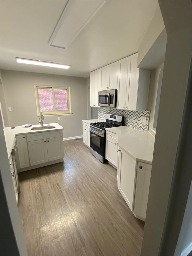 kitchen featuring appliances with stainless steel finishes, light hardwood / wood-style floors, kitchen peninsula, sink, and white cabinetry