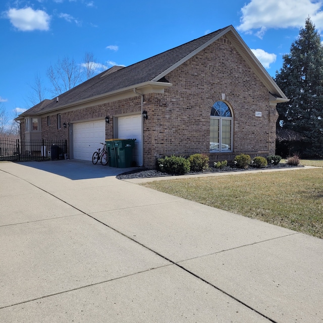 view of side of home with fence, an attached garage, concrete driveway, brick siding, and a yard