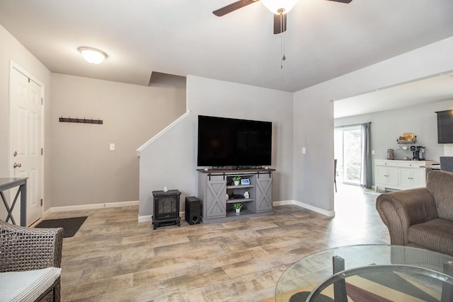 living room with ceiling fan, light wood-type flooring, and a wood stove