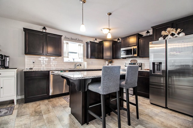 kitchen with light stone counters, a center island, appliances with stainless steel finishes, pendant lighting, and decorative backsplash