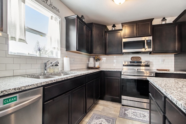 kitchen with stainless steel appliances, sink, light stone counters, and decorative backsplash