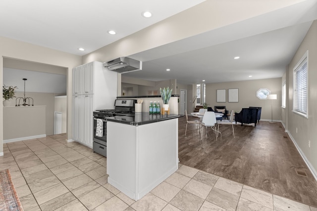 kitchen with kitchen peninsula, range hood, stainless steel range with gas cooktop, white cabinetry, and light tile patterned flooring