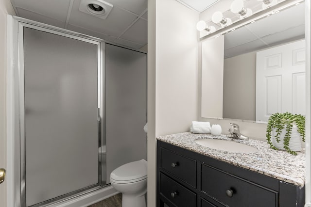 bathroom with toilet, a shower with door, a drop ceiling, and vanity