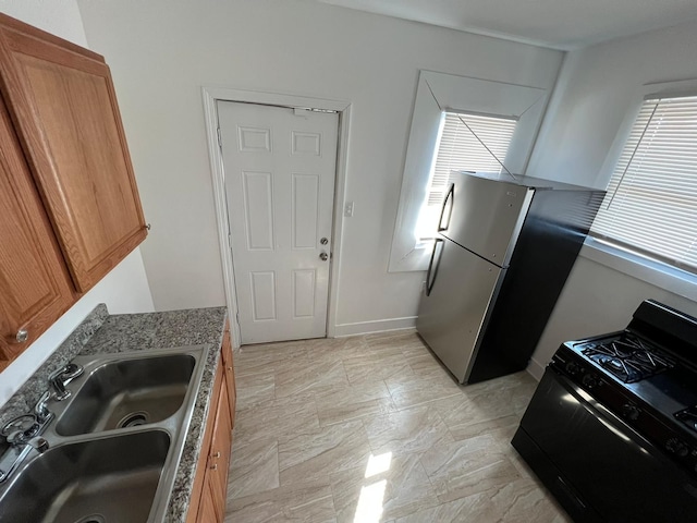 kitchen with sink, light stone countertops, black range with gas cooktop, and stainless steel fridge