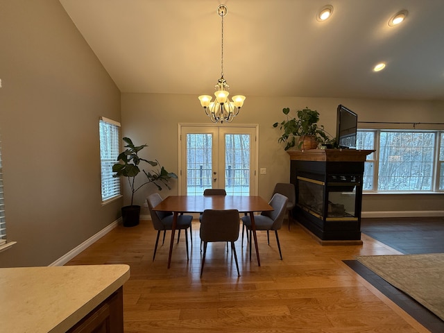 dining area featuring a multi sided fireplace, wood-type flooring, lofted ceiling, and a chandelier