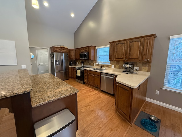 kitchen with appliances with stainless steel finishes, sink, light wood-type flooring, high vaulted ceiling, and a breakfast bar