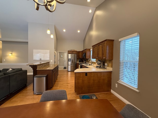 kitchen with kitchen peninsula, an inviting chandelier, light wood-type flooring, high vaulted ceiling, and stainless steel fridge