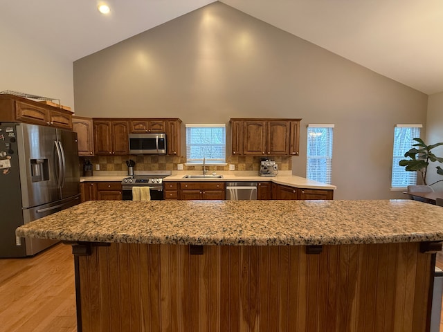 kitchen with tasteful backsplash, light hardwood / wood-style floors, sink, stainless steel appliances, and high vaulted ceiling