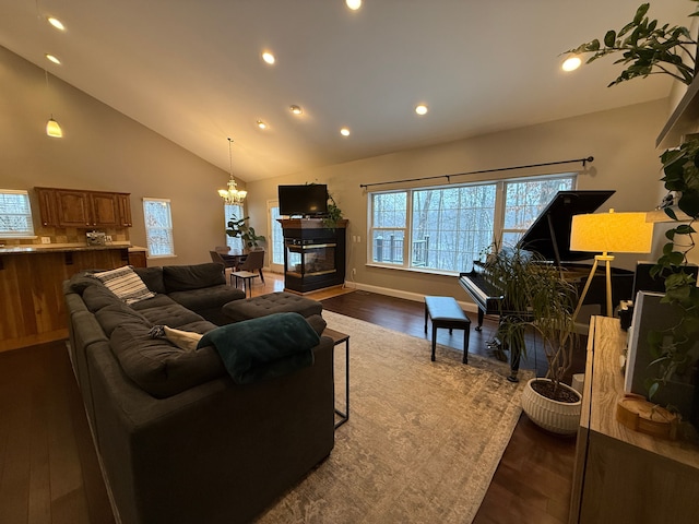 living room featuring high vaulted ceiling, a tiled fireplace, dark wood-type flooring, and a notable chandelier