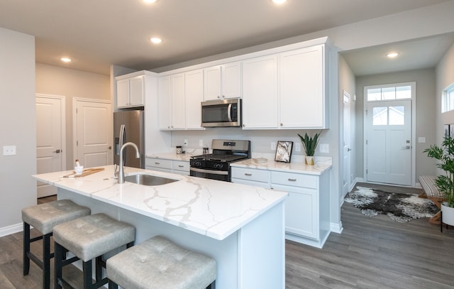 kitchen with sink, stainless steel appliances, white cabinetry, and a kitchen island with sink