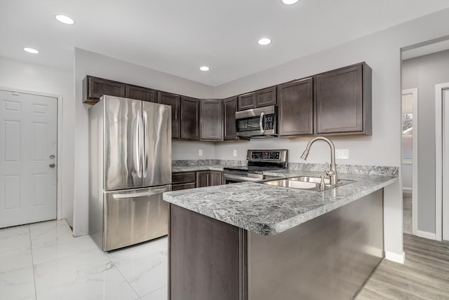 kitchen featuring sink, appliances with stainless steel finishes, dark brown cabinetry, light stone counters, and kitchen peninsula