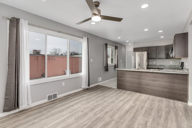 kitchen with dark brown cabinets, light hardwood / wood-style flooring, kitchen peninsula, stainless steel appliances, and light stone countertops