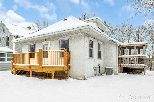 snow covered back of property with central AC unit, a sunroom, and a wooden deck