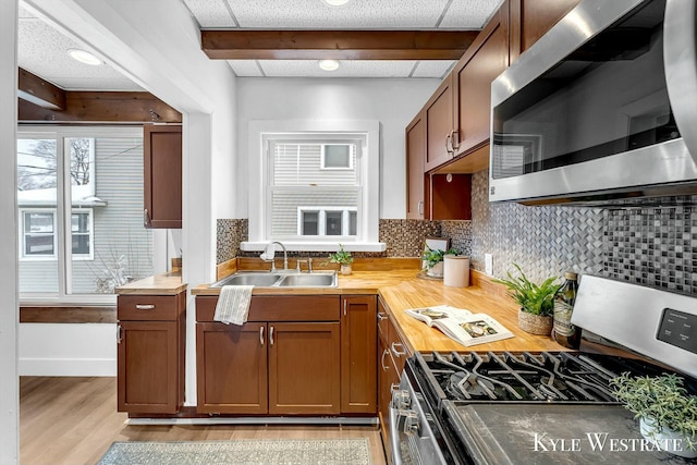 kitchen with stainless steel appliances, sink, light wood-type flooring, decorative backsplash, and wooden counters