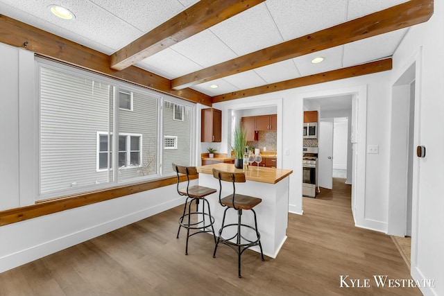 kitchen featuring wooden counters, a breakfast bar area, appliances with stainless steel finishes, light wood-type flooring, and decorative backsplash