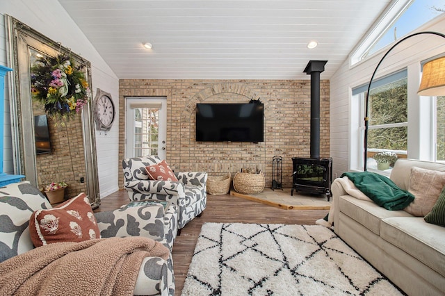 living room featuring brick wall, vaulted ceiling, wood-type flooring, and a wood stove