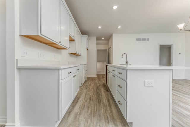 kitchen with sink, a center island with sink, white cabinetry, and light hardwood / wood-style floors