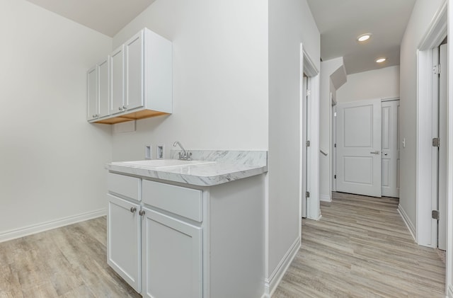 interior space with sink, light hardwood / wood-style floors, hookup for a washing machine, and cabinets