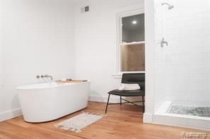 full bathroom featuring a shower stall, wood finished floors, baseboards, and a freestanding bath