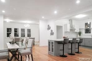 kitchen featuring a kitchen bar, white cabinetry, light wood-type flooring, gray cabinets, and wall chimney range hood