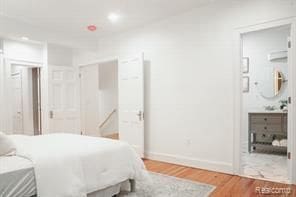 bedroom featuring wood finished floors, baseboards, and connected bathroom