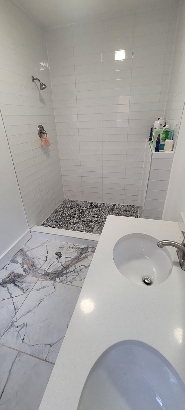 full bathroom featuring a sink, marble finish floor, and a tile shower