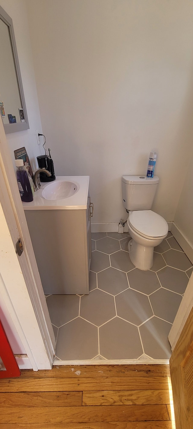 half bath with baseboards, toilet, vanity, and tile patterned flooring