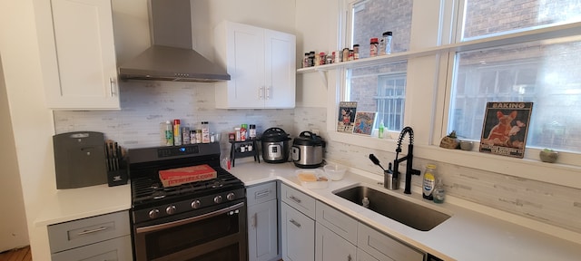 kitchen featuring decorative backsplash, wall chimney exhaust hood, stainless steel range with gas cooktop, and a sink