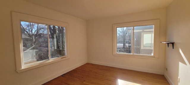 unfurnished room with plenty of natural light, baseboards, and wood finished floors