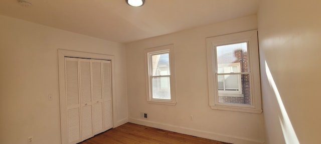 unfurnished bedroom featuring baseboards, multiple windows, a closet, and wood finished floors