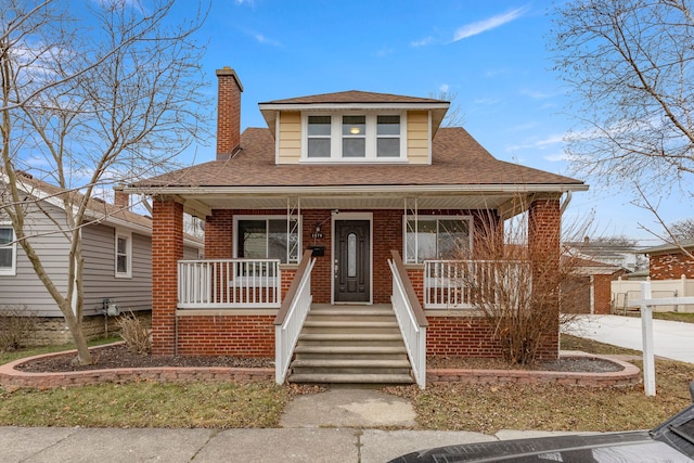 bungalow-style home with a porch, brick siding, a chimney, and roof with shingles