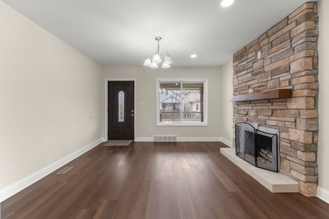 entryway featuring dark wood-style flooring, visible vents, a stone fireplace, and an inviting chandelier