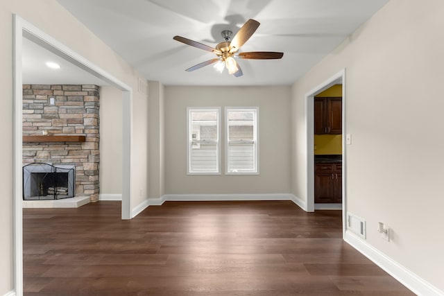 unfurnished living room with ceiling fan, visible vents, a fireplace, baseboards, and dark wood-type flooring