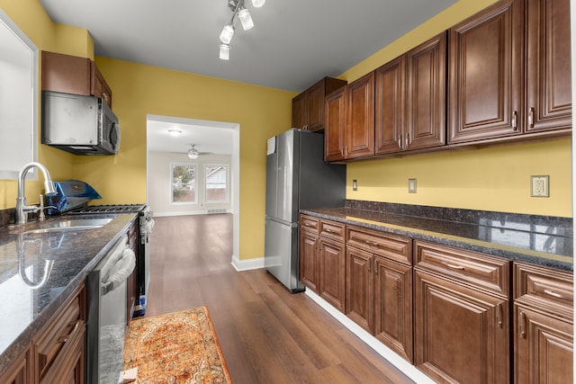 kitchen with dark hardwood / wood-style floors, dark stone counters, appliances with stainless steel finishes, ceiling fan, and sink