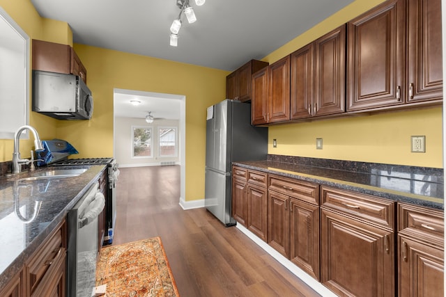 kitchen with a ceiling fan, dark wood-type flooring, dark stone counters, a sink, and appliances with stainless steel finishes