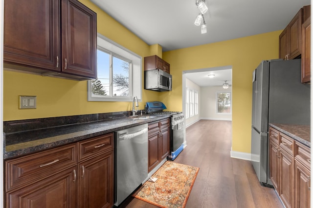 kitchen with dark wood-style flooring, appliances with stainless steel finishes, a sink, baseboards, and dark stone countertops