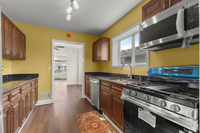 kitchen featuring sink, dark stone counters, dark hardwood / wood-style floors, rail lighting, and appliances with stainless steel finishes