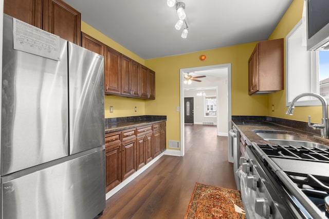 kitchen with brown cabinetry, a ceiling fan, dark wood finished floors, a sink, and stainless steel appliances