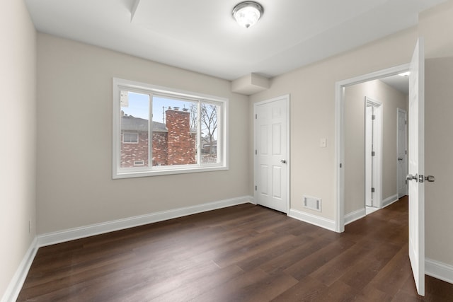 unfurnished room with baseboards, dark wood-style floors, and visible vents