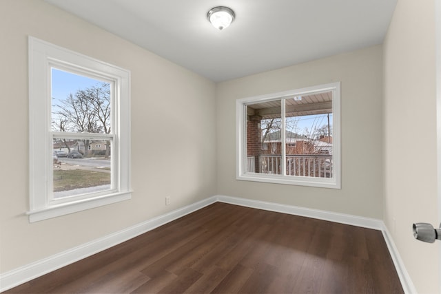 spare room with baseboards, plenty of natural light, and dark wood finished floors